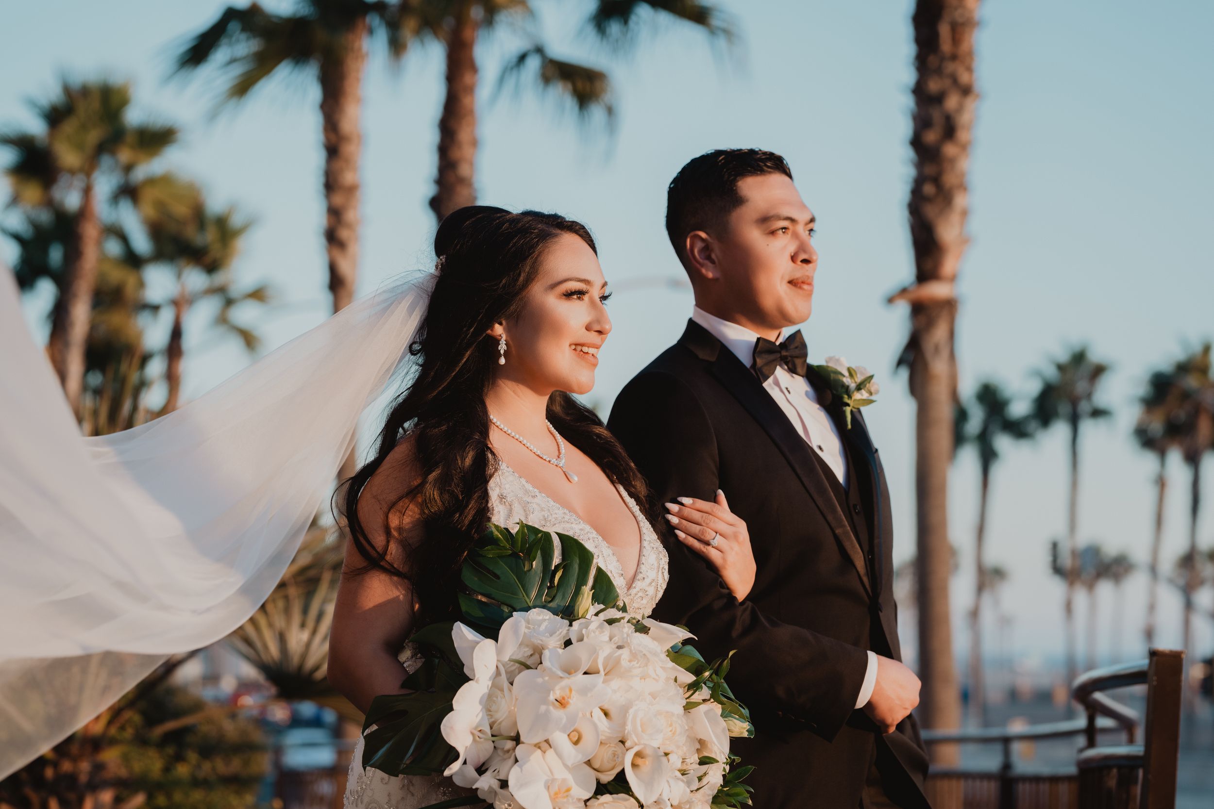 Wedding couple walking together under palm trees at sunset by the beach.