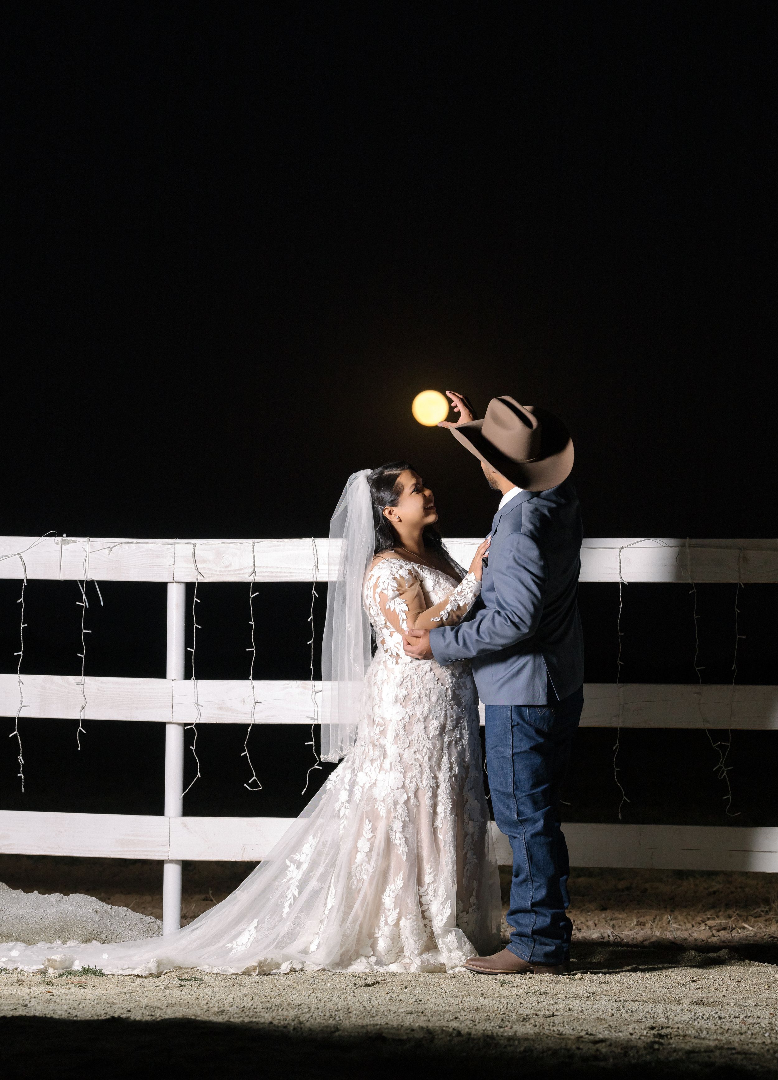 Romantic nighttime portrait of couple by white fence with moonlit sky.