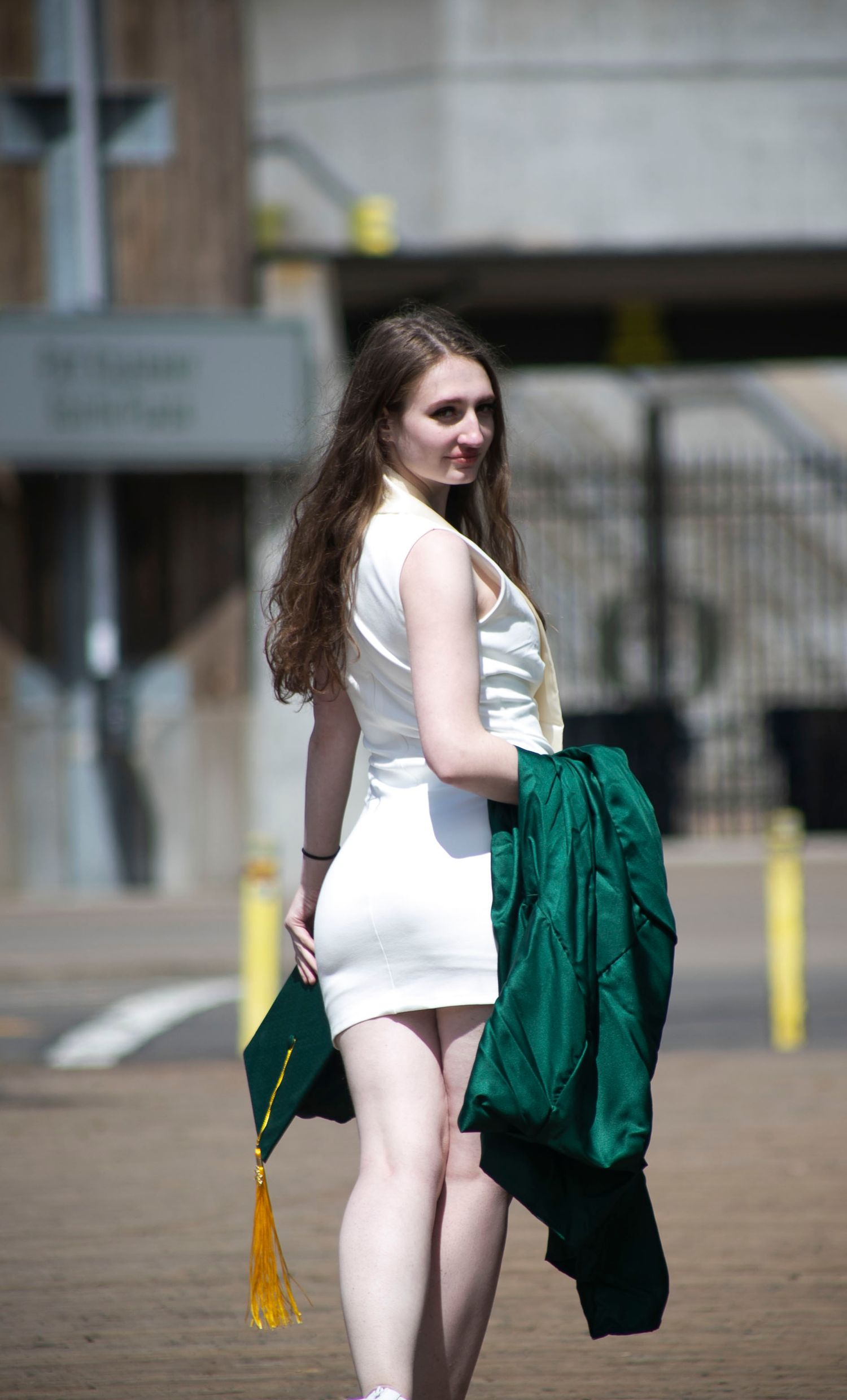 University of Oregon senior, looking over her shoulder with graduation robe and cap, in front of Autzen Stadium
