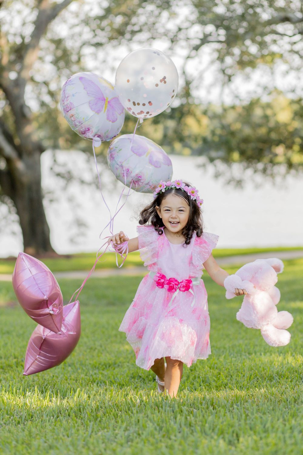 Pink dress and balloons create magical moment in sunny outdoor setting.