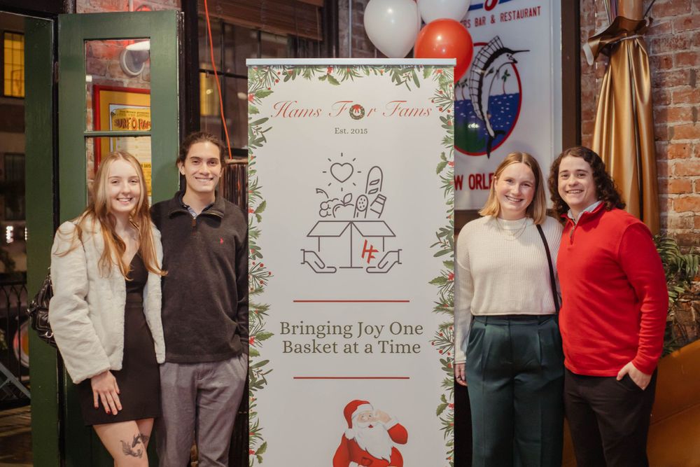 Four people stand beside a decorative holiday banner with line art illustrations in a cozy indoor setting.