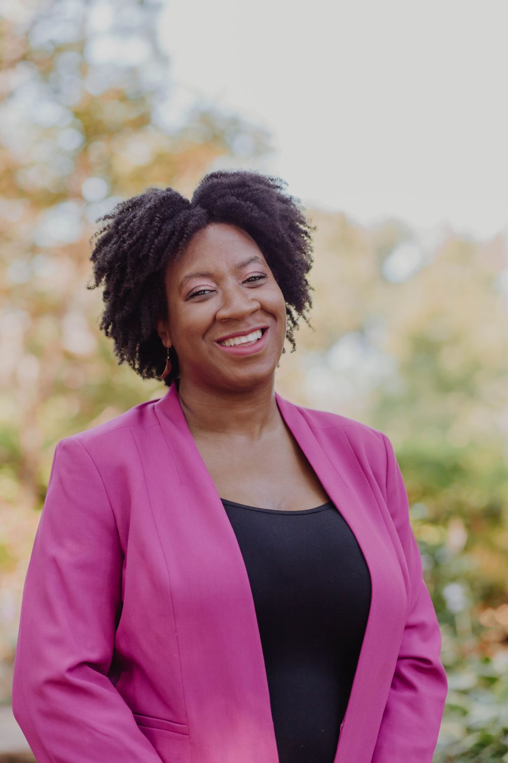 Professional headshot featuring bright pink blazer and natural hair styling.