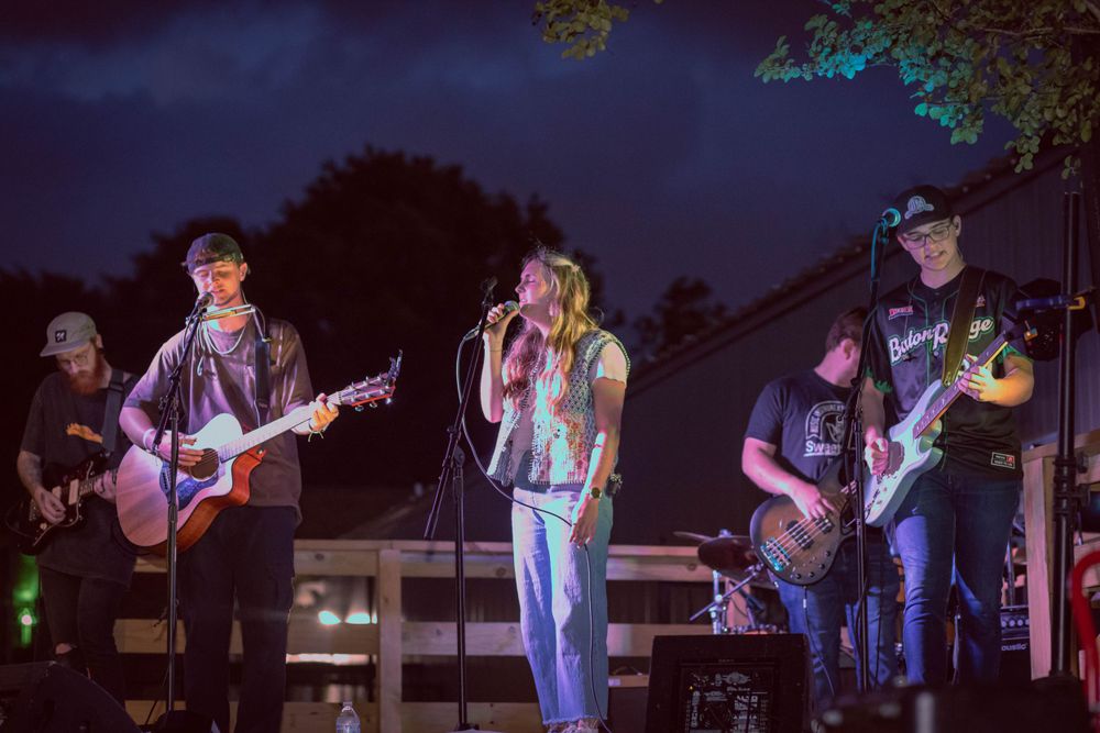 Band performing live on outdoor stage with guitars and microphones under night sky.