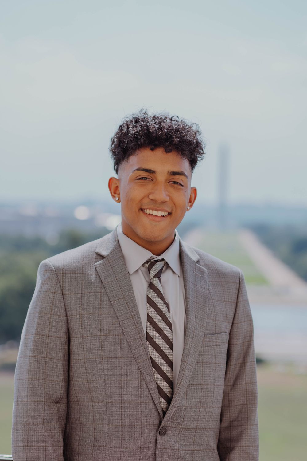 Professional headshot against blurred cityscape background with Washington Monument visible.