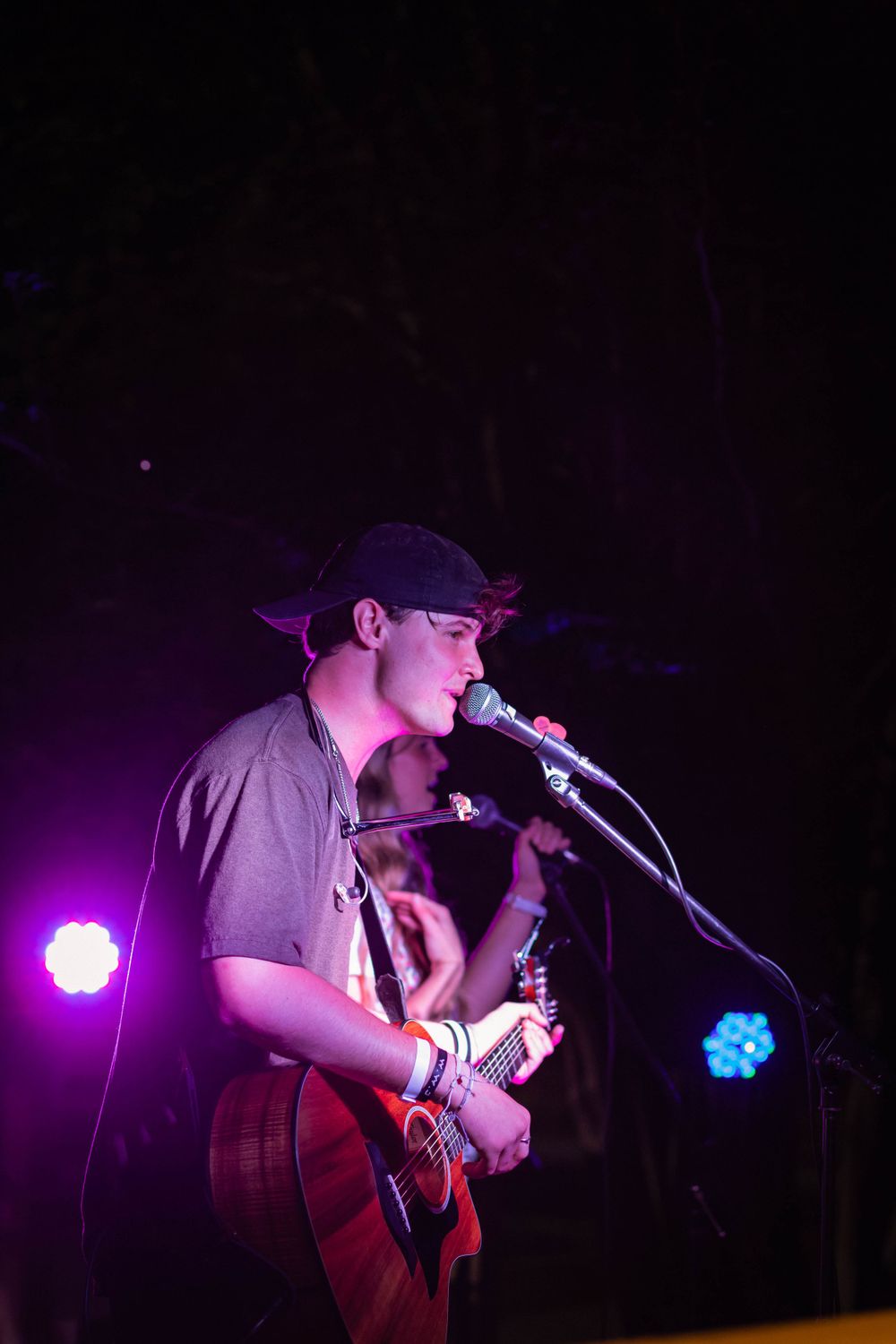 Musician singing and playing acoustic guitar under purple stage lighting at night.