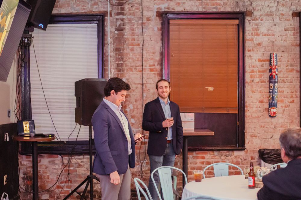 Two people standing in conversation at an event space with exposed brick walls and industrial decor.