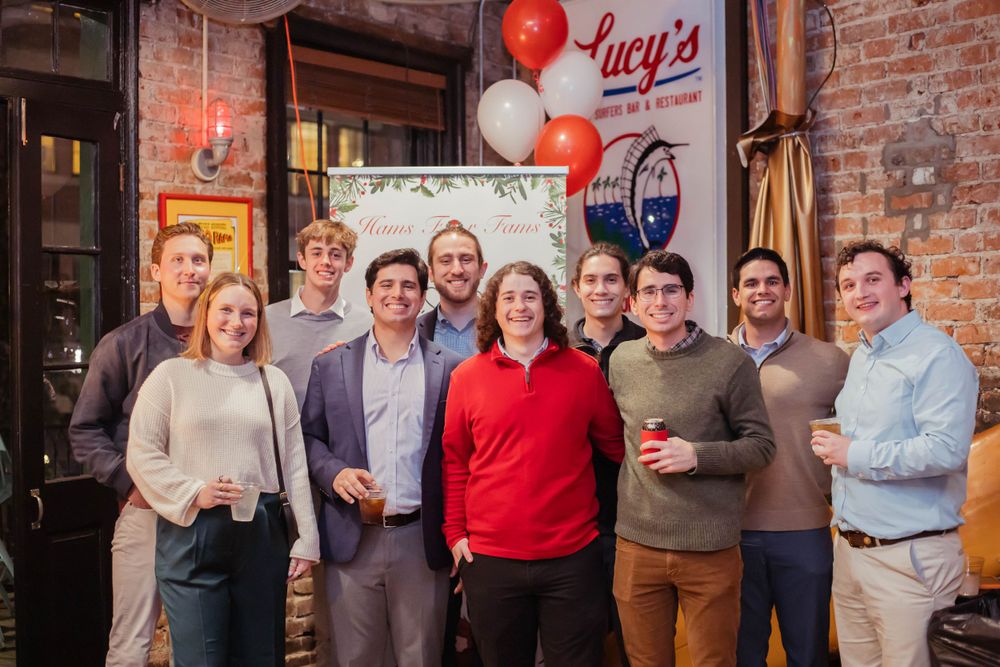 A group of people posing together for a photo in front of a brick wall with red and white balloons.