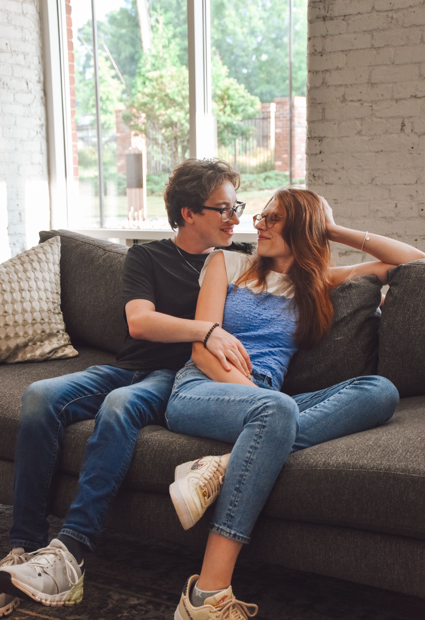 Couple relaxing on grey couch in casual attire sharing intimate moment.