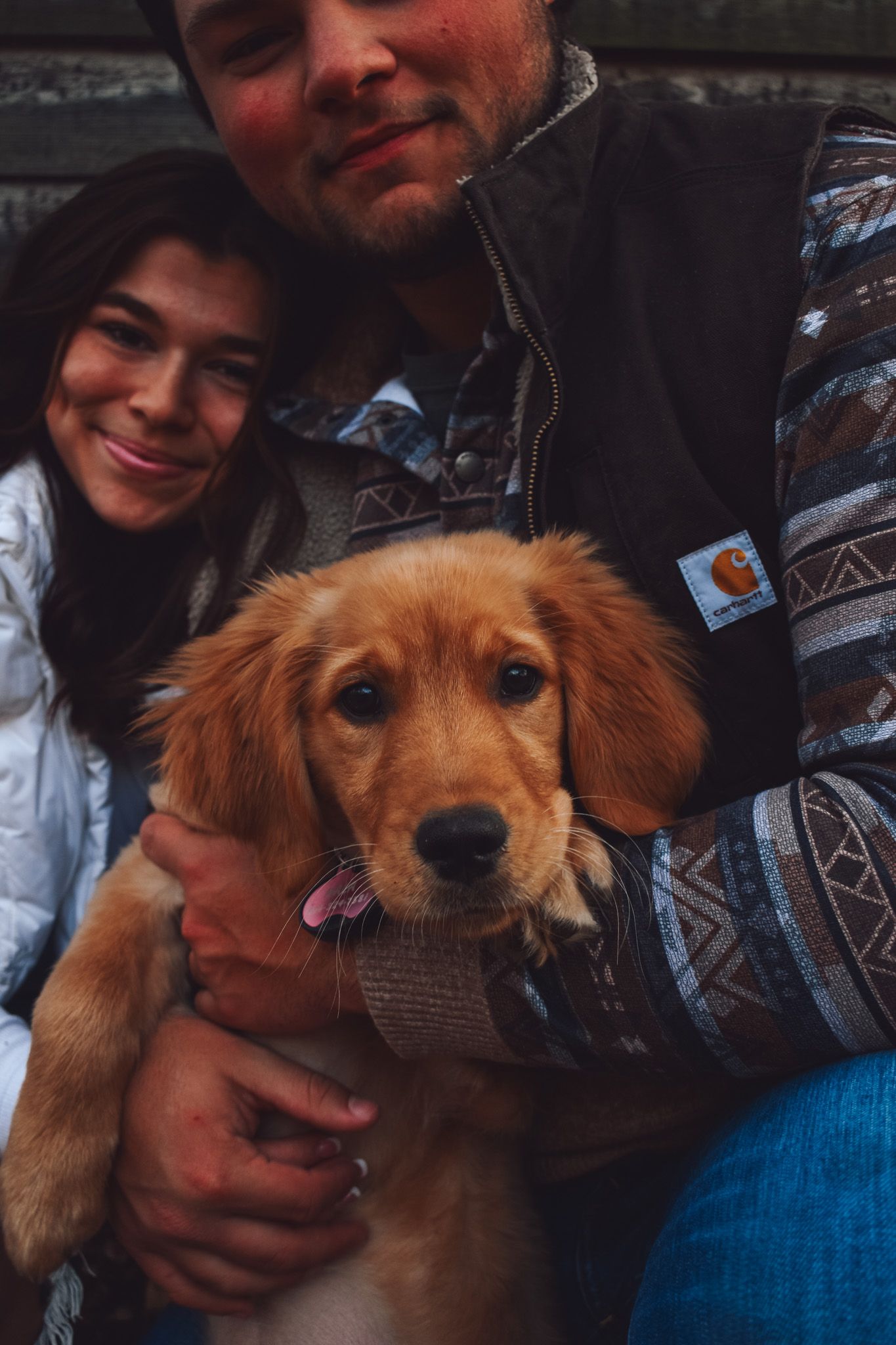Golden retriever puppy being held and cuddled by owners in casual winter attire.
