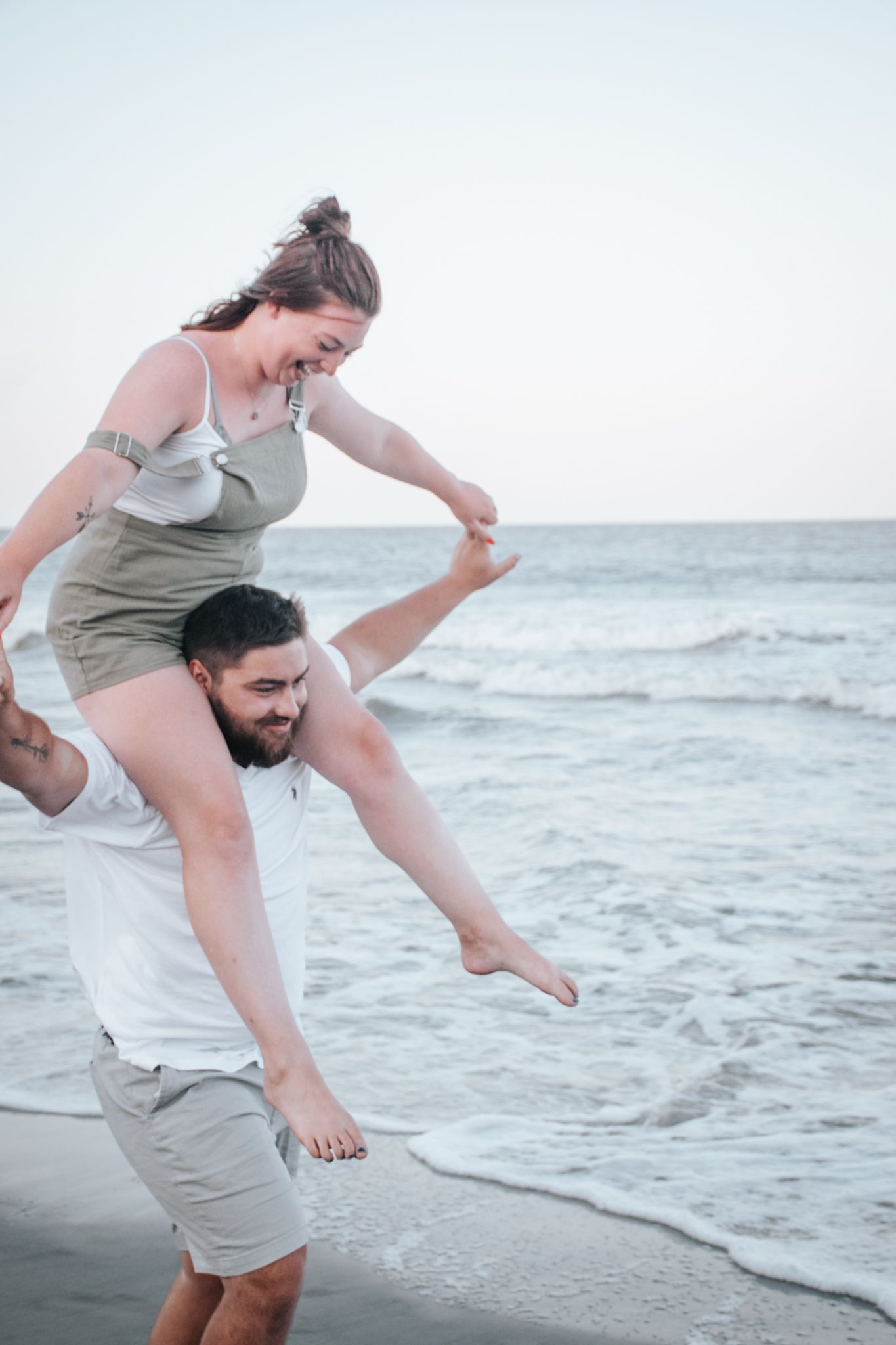 Couple playing and laughing together on sandy beach at sunset.