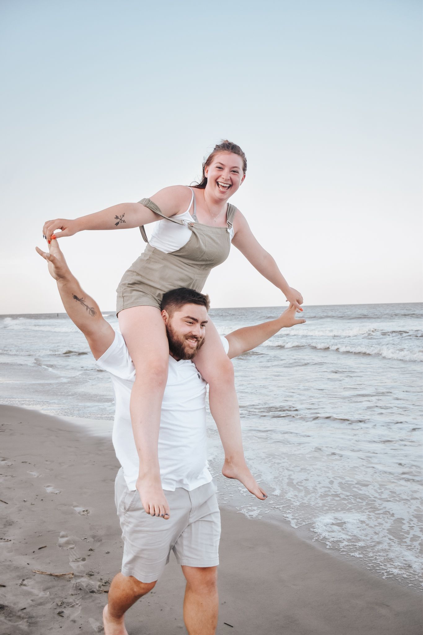 Playful couple having fun at the beach with piggyback ride against ocean backdrop.
