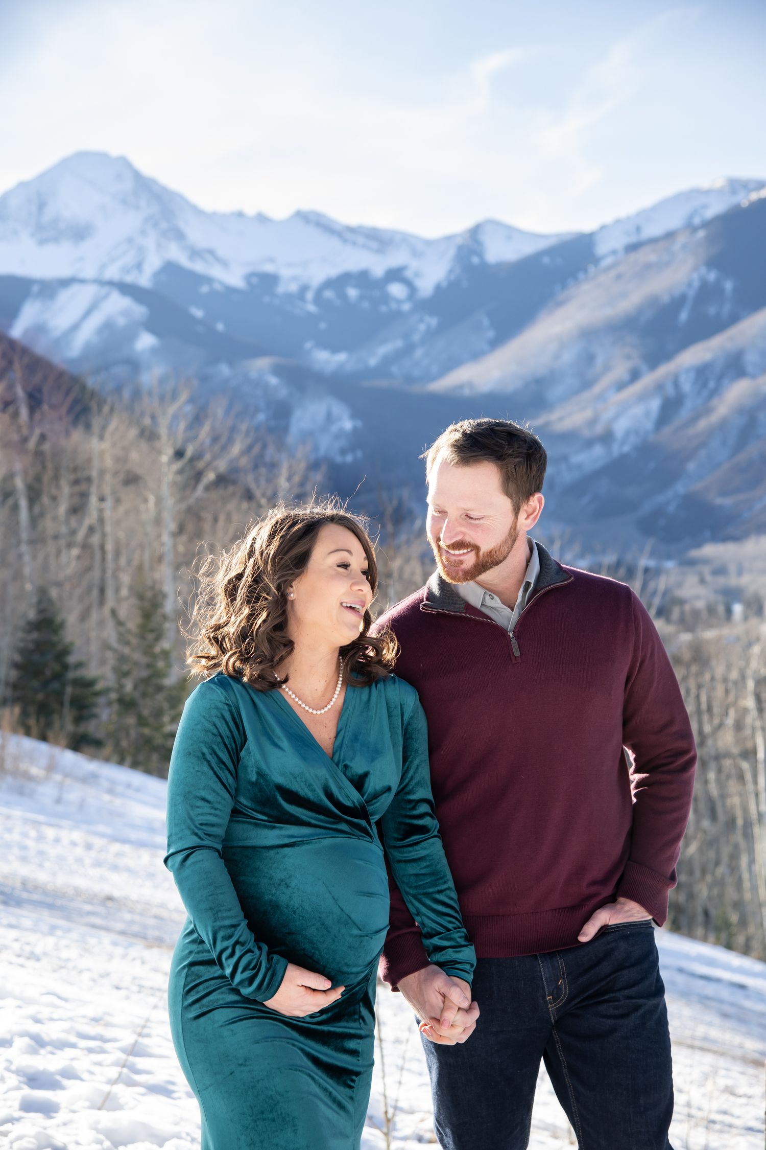 A beautiful couple walks candidly together through the snow during a winter maternity photo session in Aspen Colorado