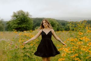Young woman in black sundress twirls joyfully among yellow wildflowers in misty hillside meadow.