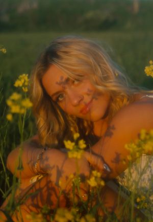 Blonde woman sitting among yellow wildflowers in a field at golden hour.
