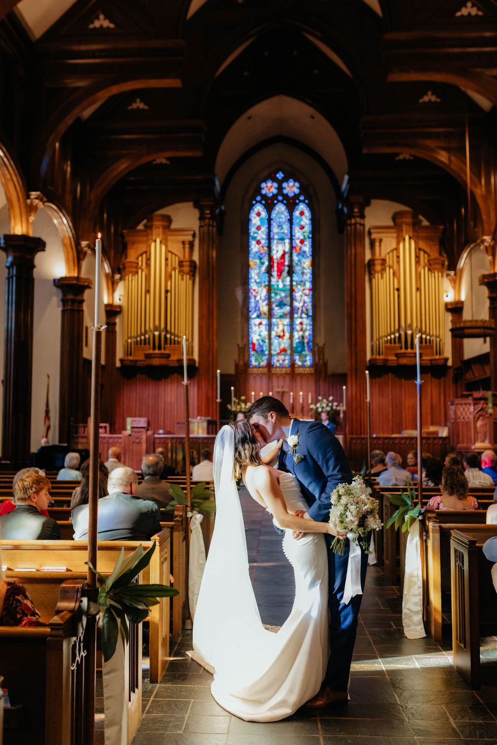 A romantic church wedding ceremony unfolds in a beautiful Gothic sanctuary with stained glass windows and wooden pews.