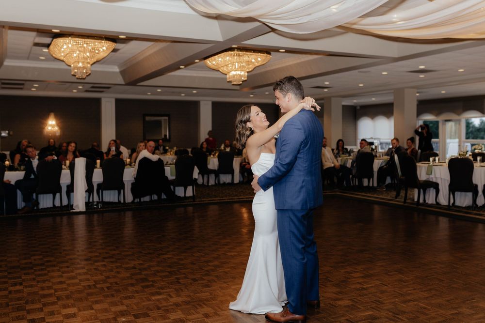 A couple shares their first dance at an elegant wedding reception under crystal chandeliers on a dark wood dance floor.