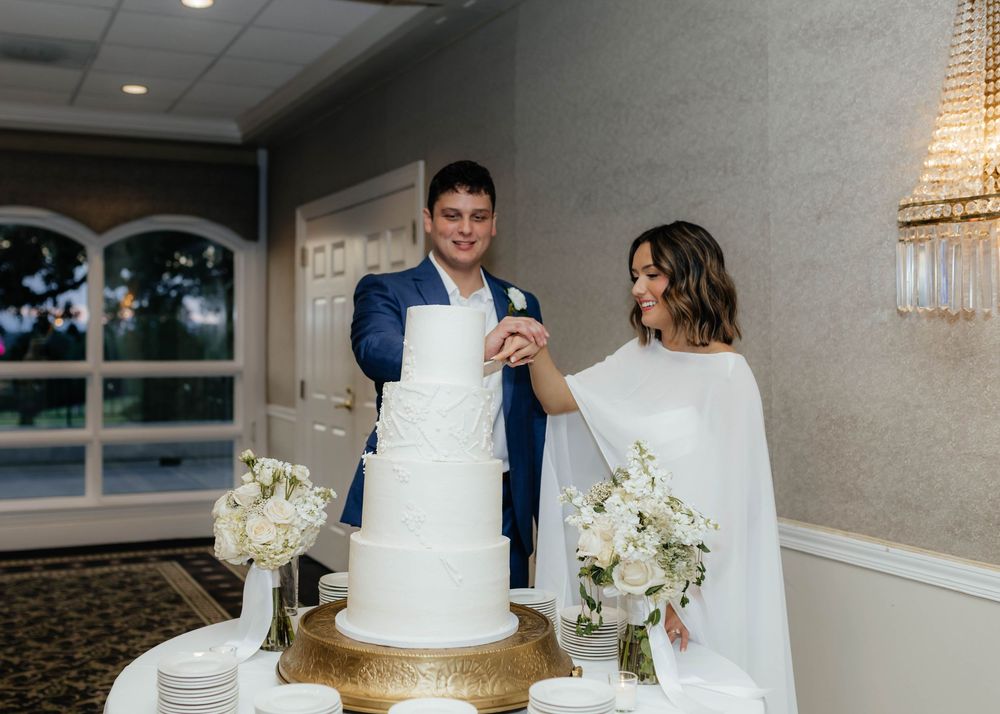 A row of elegant white wedding cakes displayed at a reception with floral decorations and soft lighting.