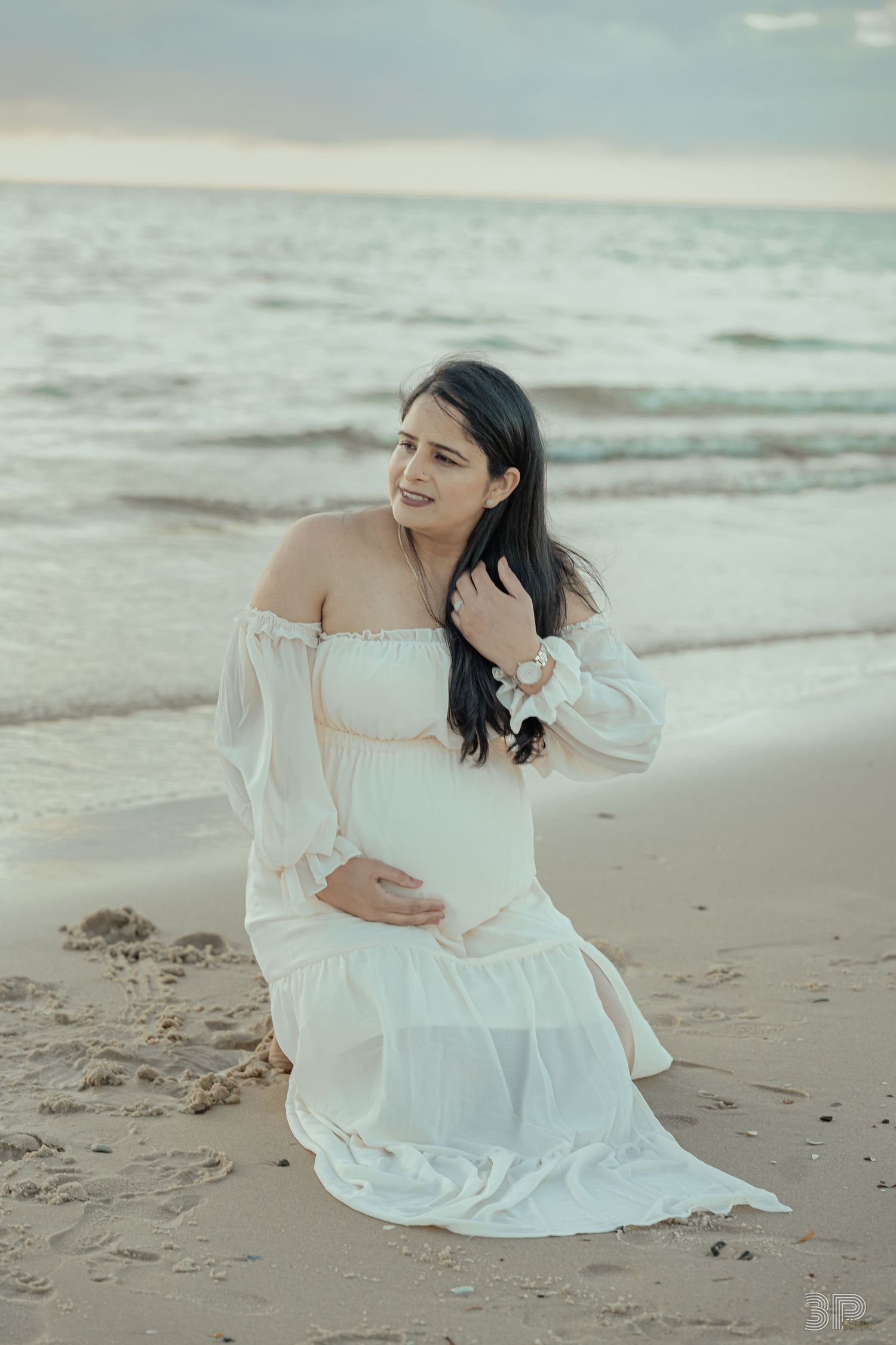 A tender moment captured at sunset on a beach with people wearing white dresses against a cloudy sky.