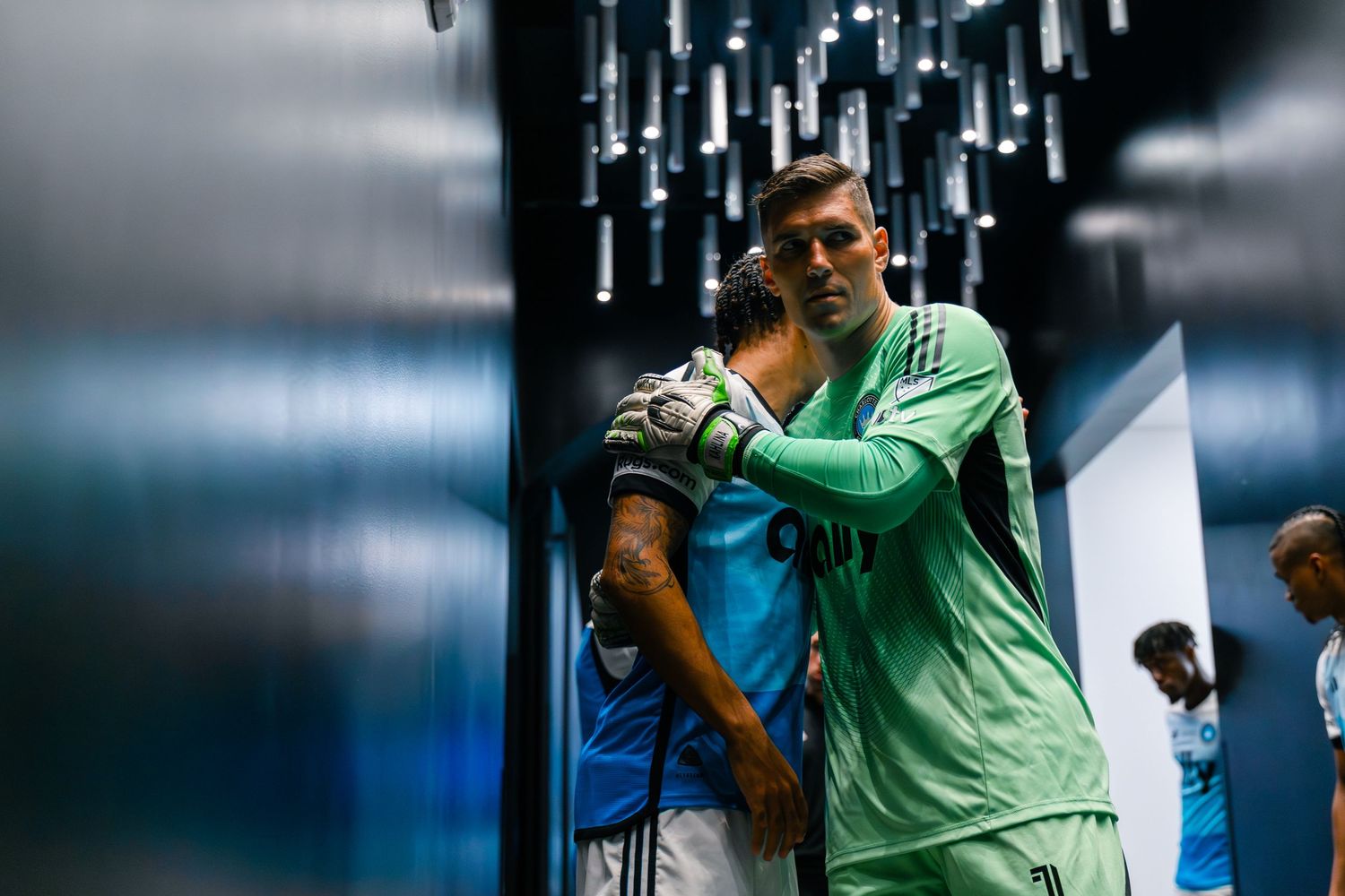 Two soccer players share an embrace in a stadium tunnel before or after a match.