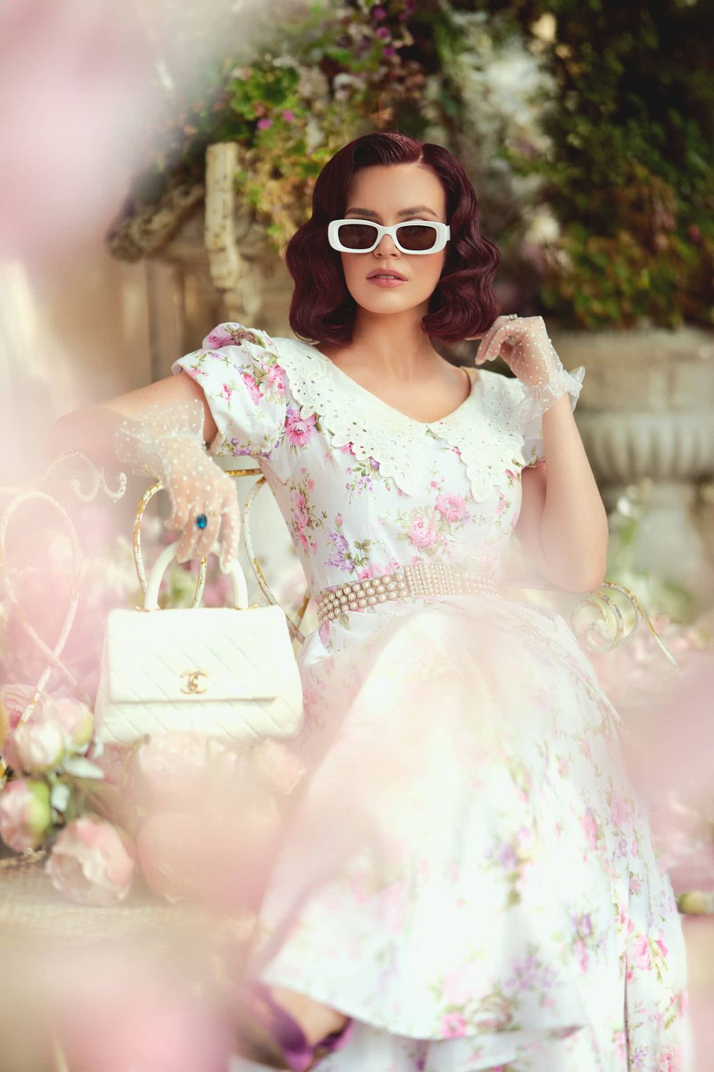 Dreamy garden photoshoot featuring white floral dress and retro sunglasses amid pink blooms.