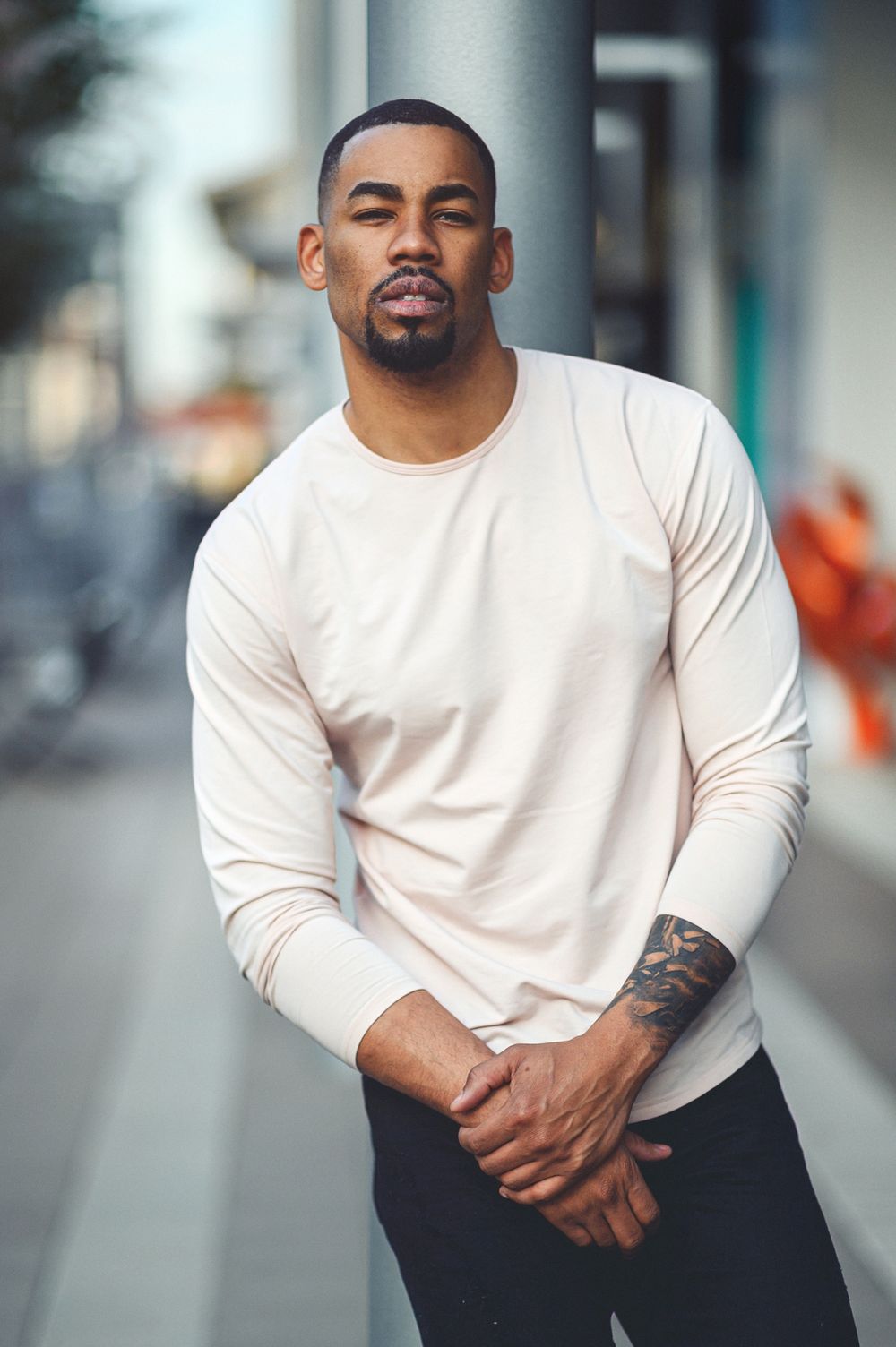 Man in white long sleeve shirt poses on urban street in casual fashion photoshoot.