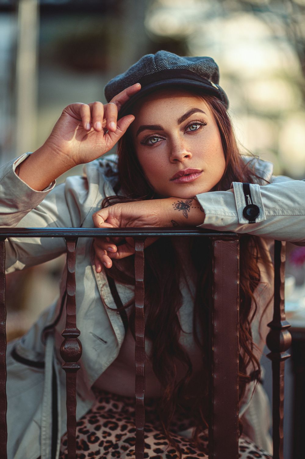 Fashion portrait of model in casual attire leaning on wooden railing with blurred background.