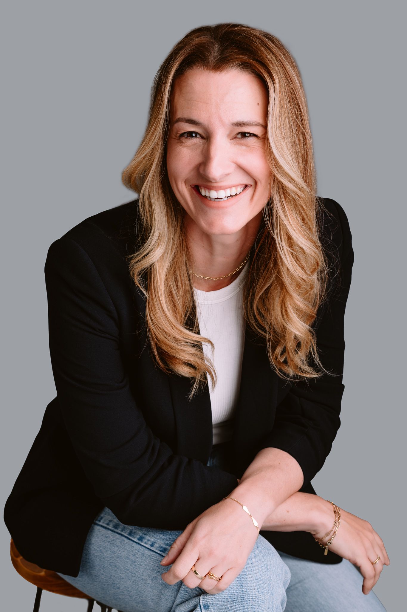Professional studio portrait of a woman in black blazer and white shirt against grey background.