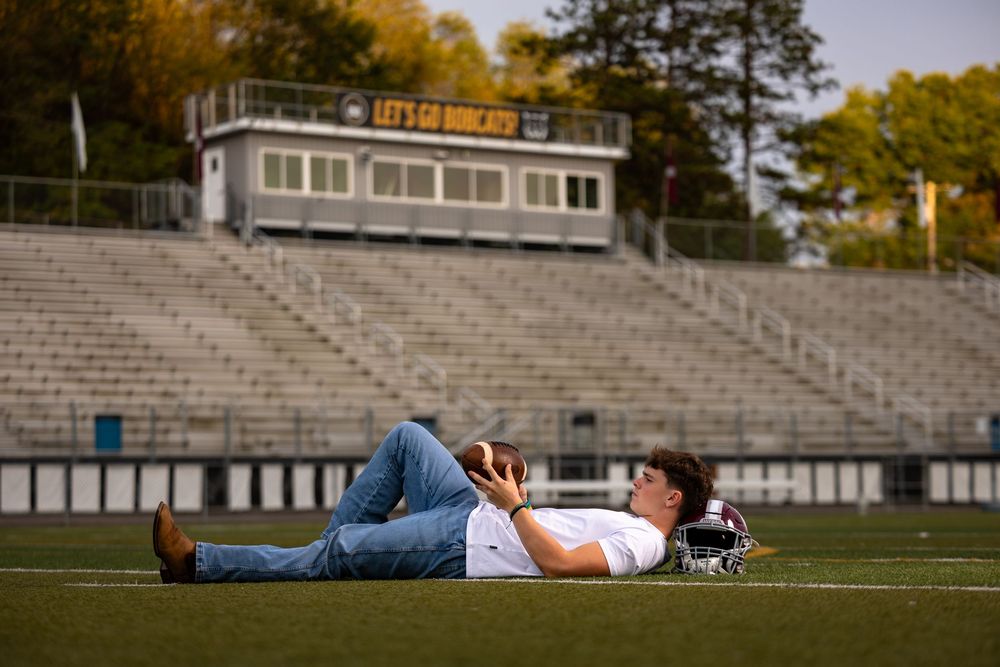A person lies on a football field with their hands behind their head during golden hour lighting.
