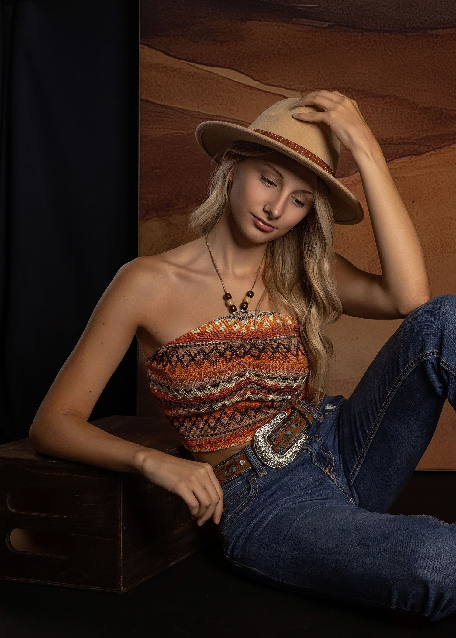 Western-style portrait featuring strapless tribal print top, cowboy hat, and denim in warm brown tones.