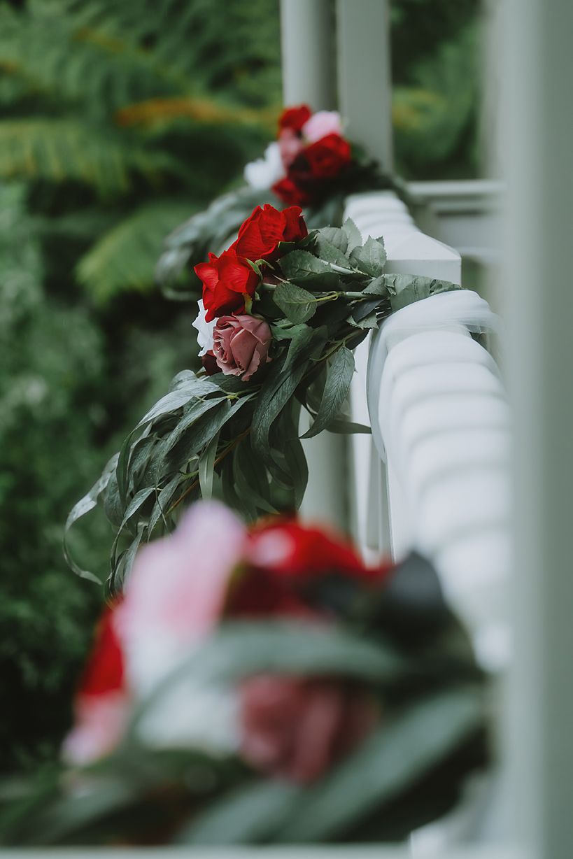 Red roses and foliage create a romantic blur against white pillars in soft focus.
