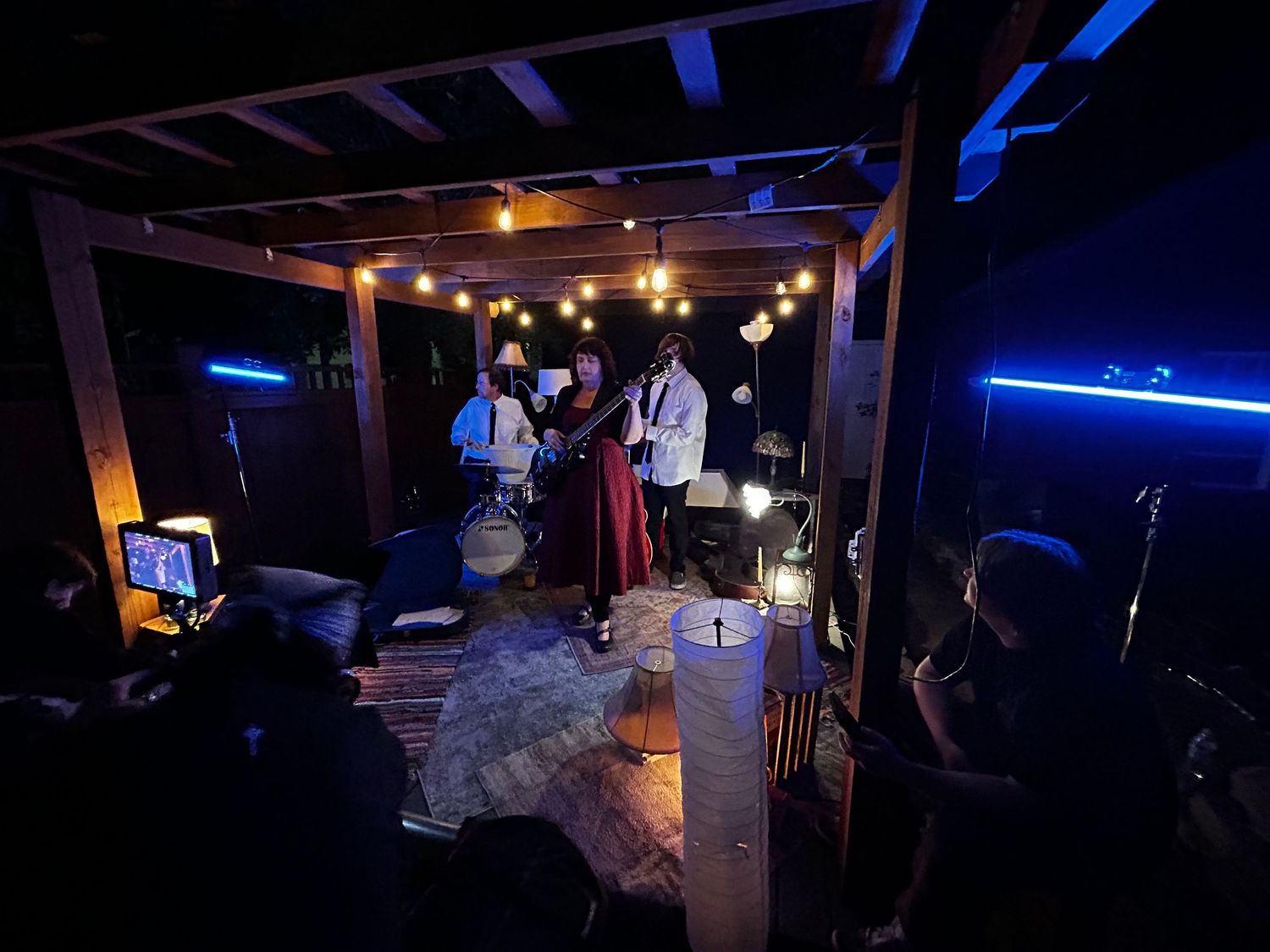 Musicians perform under string lights at an outdoor patio venue during a nighttime performance.