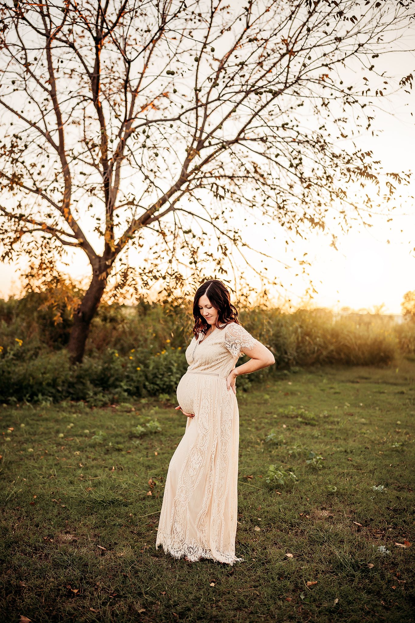 A series of sunset maternity photos showing a woman in a flowing white lace dress standing in a grassy field under trees.
