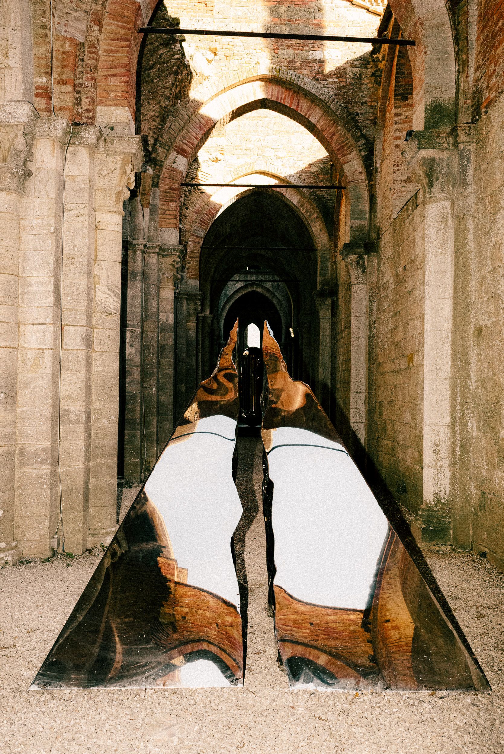Ancient stone arches and columns line a historic monastery corridor with dramatic lighting and shadows.