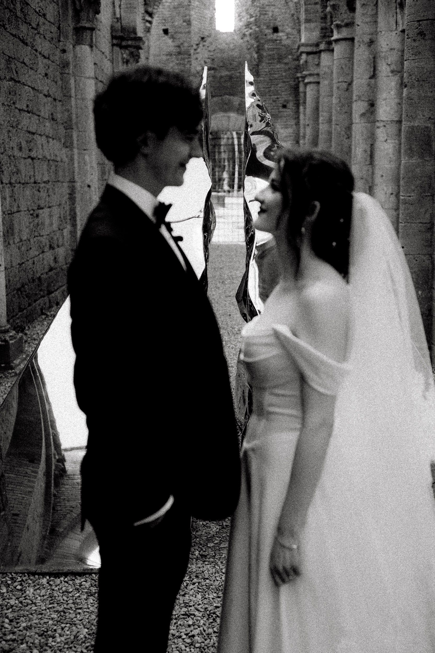 Black and white wedding photos showing a couple in formal attire posing against a stone wall in an elegant setting.