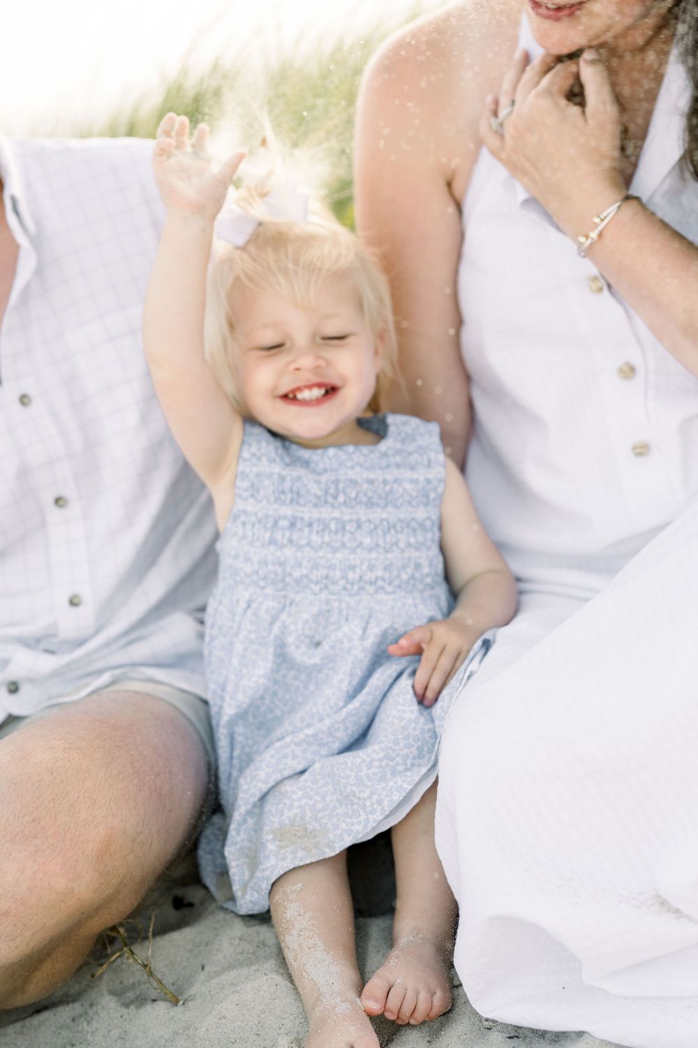 Family wearing white and light blue clothing sits together in a casual outdoor photo session.