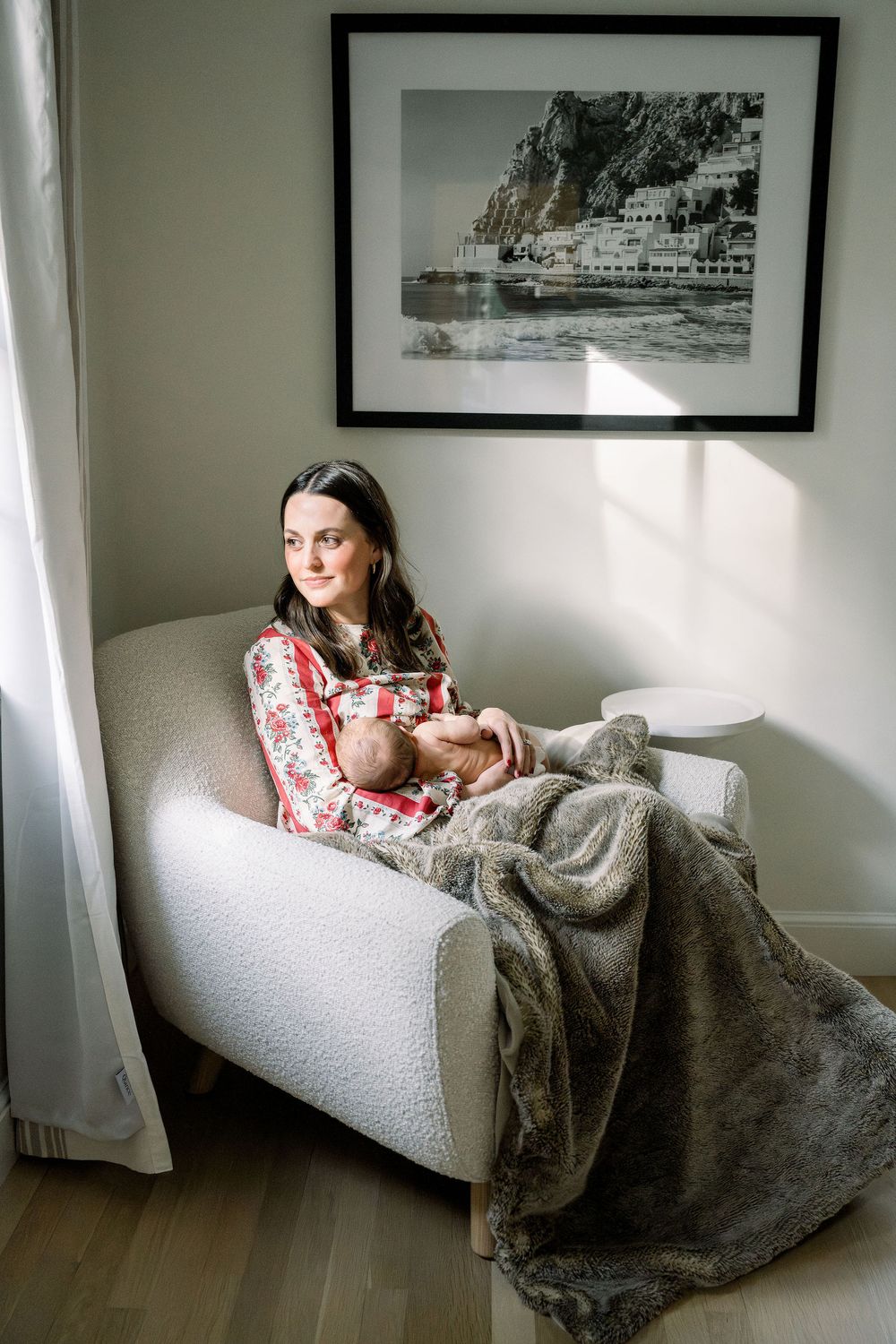 A person relaxes on a white couch with a cozy gray blanket while framed artwork decorates the wall behind them.