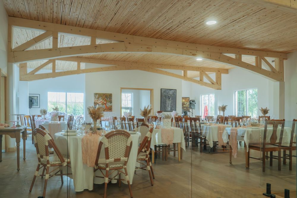 Large banquet hall with wooden beams and white tables set up for an event under warm lighting.