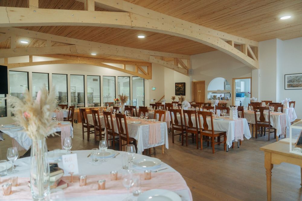 Large banquet hall with wooden beams and white tables set up for a wedding reception.