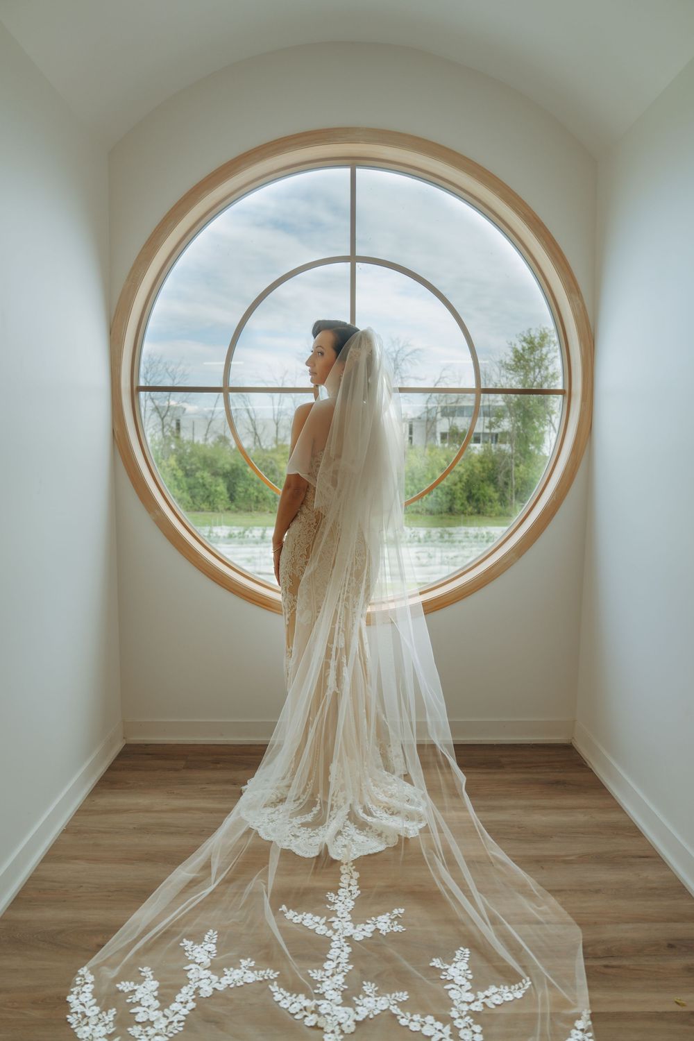 A flowing cathedral length wedding veil with delicate lace details is displayed in a room with an oval window.