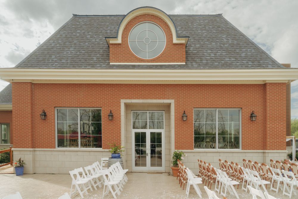 An elegant brick wedding venue with arched window and white chairs set up for an outdoor ceremony.