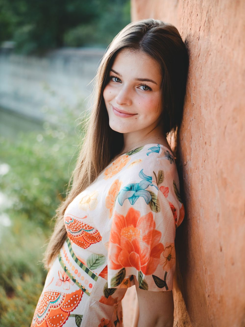 A floral dress with orange and blue flowers creates a soft and feminine silhouette against a rustic wall background.