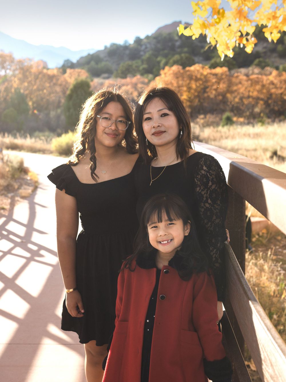 Three people pose together on a wooden walkway during autumn with golden foliage in the background.