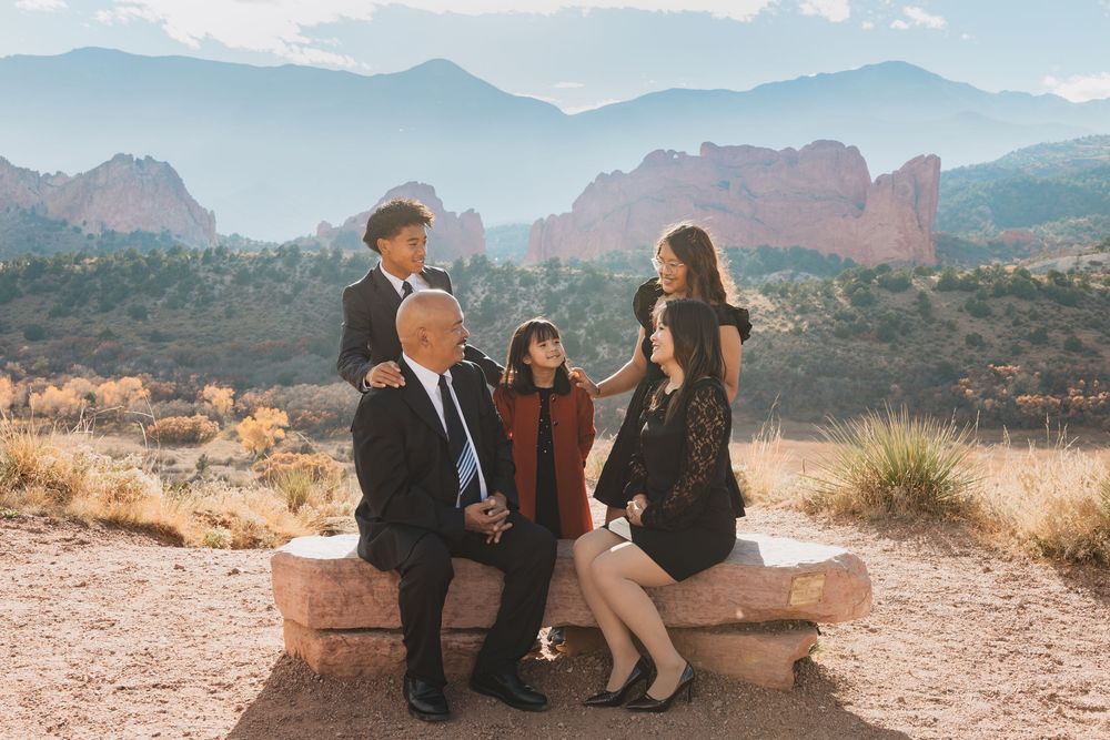 A group sits on a stone bench overlooking the scenic Garden of the Gods park in Colorado Springs during sunset.