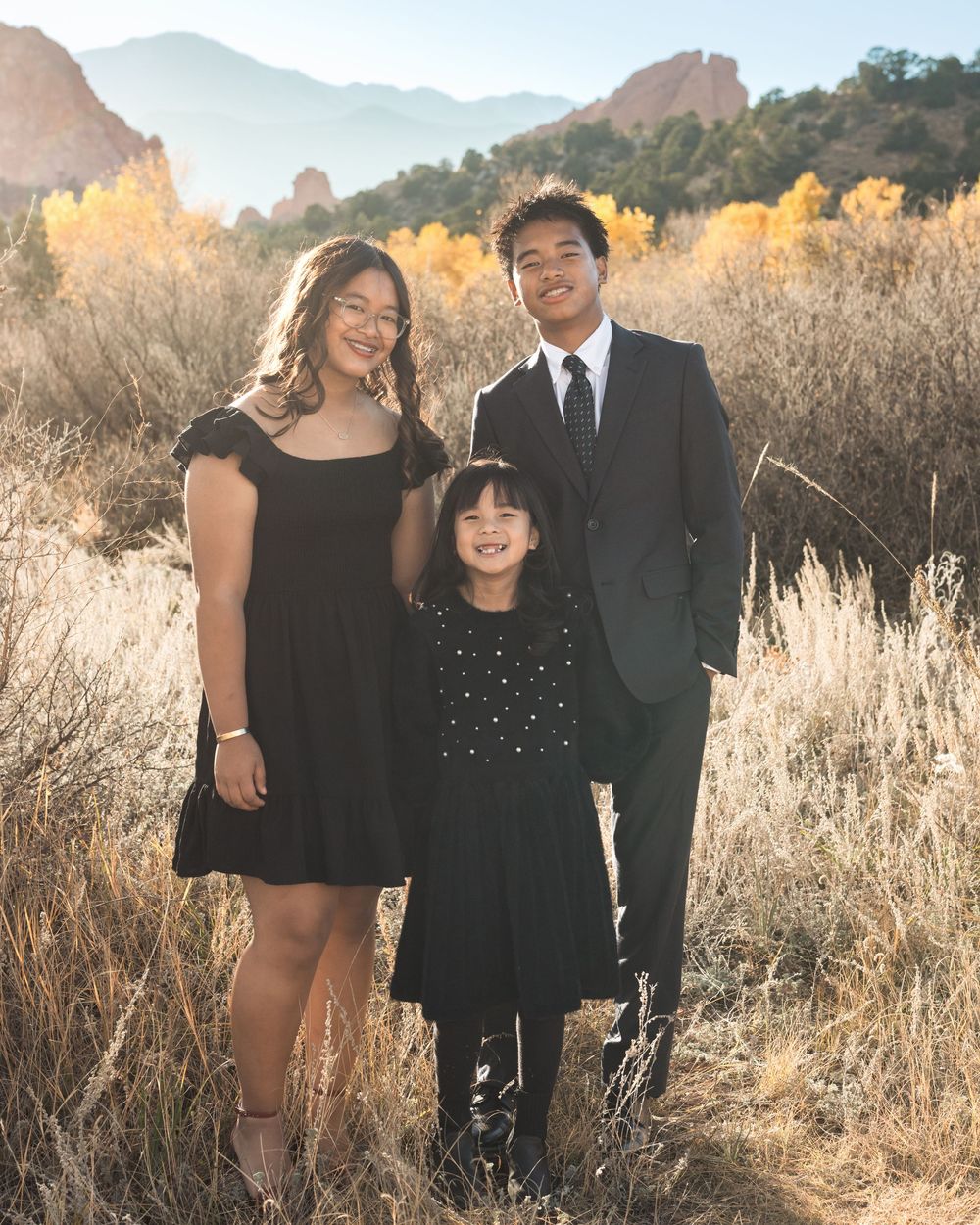 Three people pose together in tall golden grass during sunset in a natural outdoor setting.