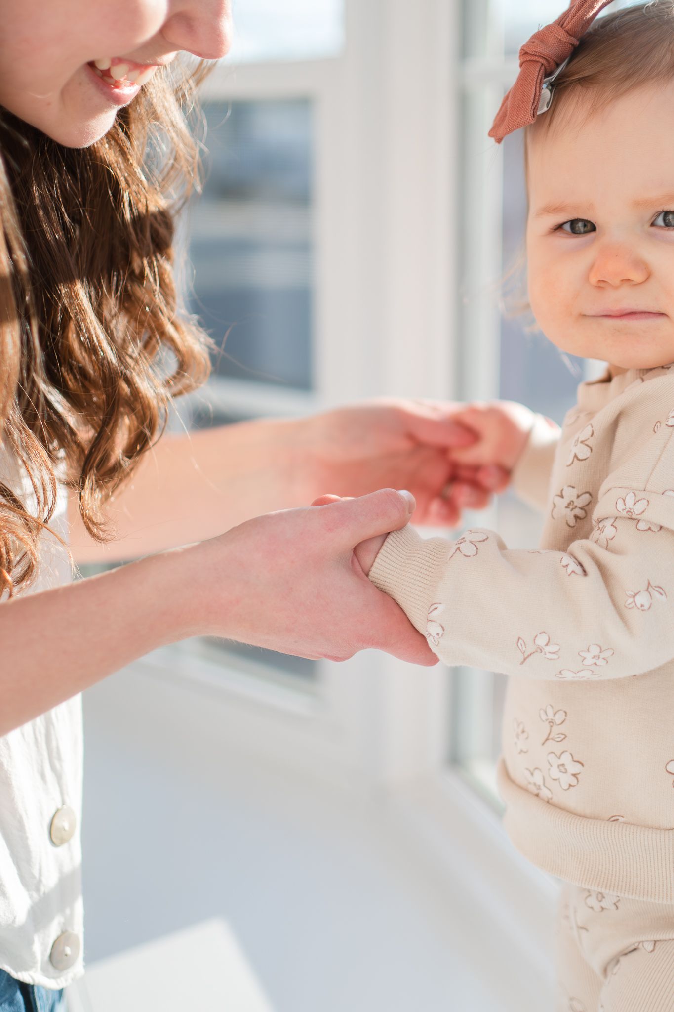 A tender moment between parent and child holding hands in soft natural light, wearing matching white floral outfits.