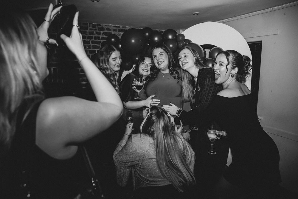 Party guests dancing and socializing in a dimly lit room with brick walls.