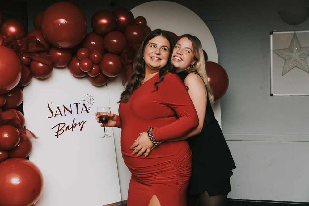 Festive baby shower session featuring red balloon garland and Santa Baby wall decor.