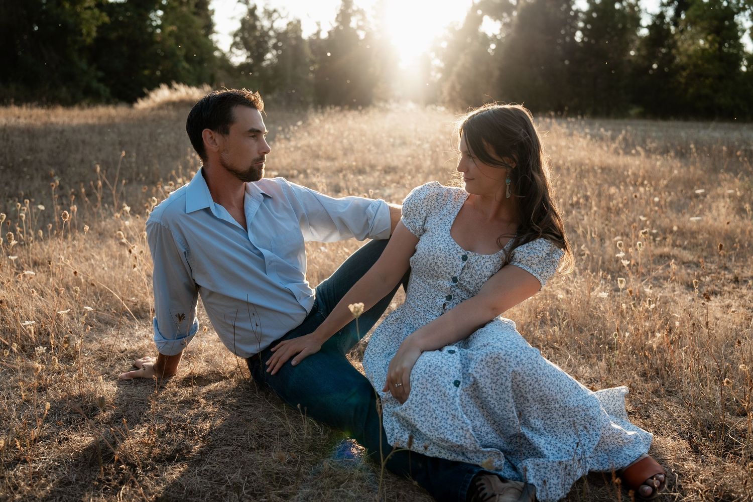 Couple embraces and laughs together in a golden wheat field at sunset.