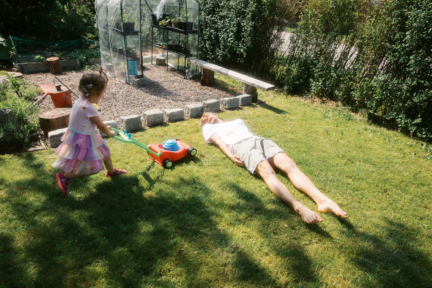 A sunny backyard scene with a toy wagon and playground equipment while people relax on the grass.