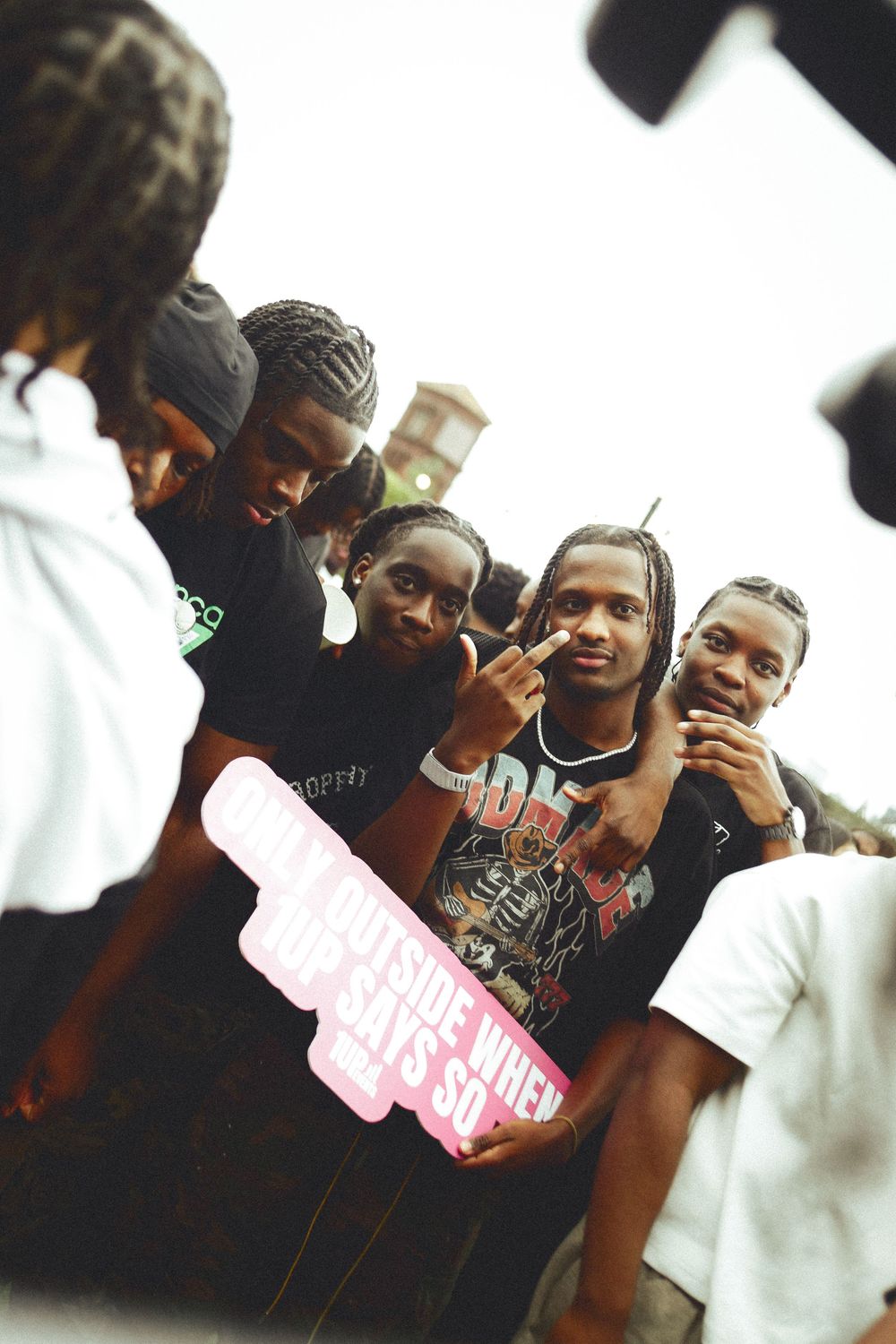 Group of young people posing together outdoors, one holding a pink sign reading outside when God says so.